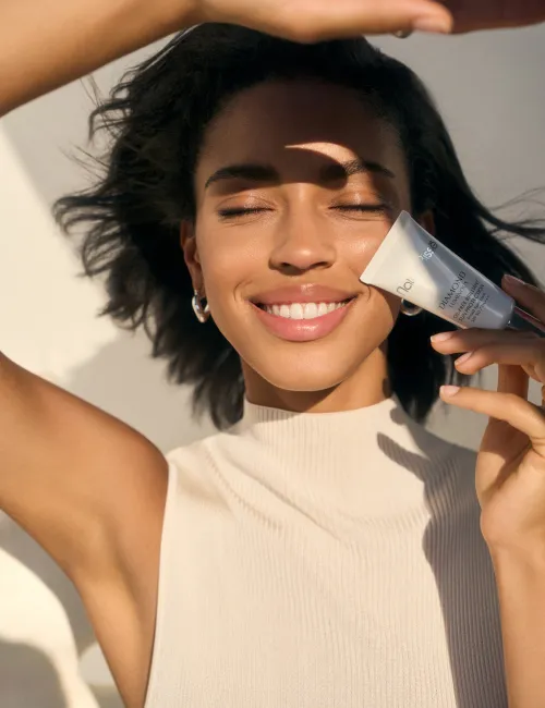 Mujer sonriendo sosteniendo la crema Essential Shock Intense en sus manos. Producto presentado en nuestros bestsellers.
