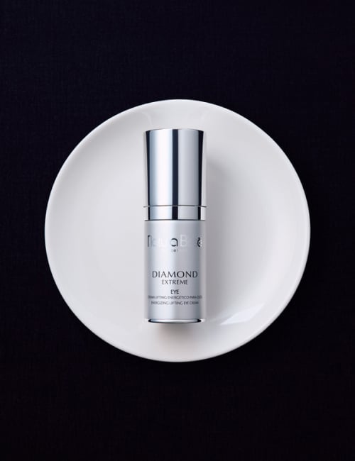 Woman with a slight smile, holding Natura Bissé's Diamond Extreme Eye cream. Skincare product featured in bestsellers.