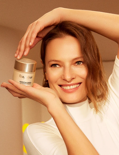 Mujer sonriendo sosteniendo la crema Essential Shock Intense en sus manos. Producto presentado en nuestros bestsellers.