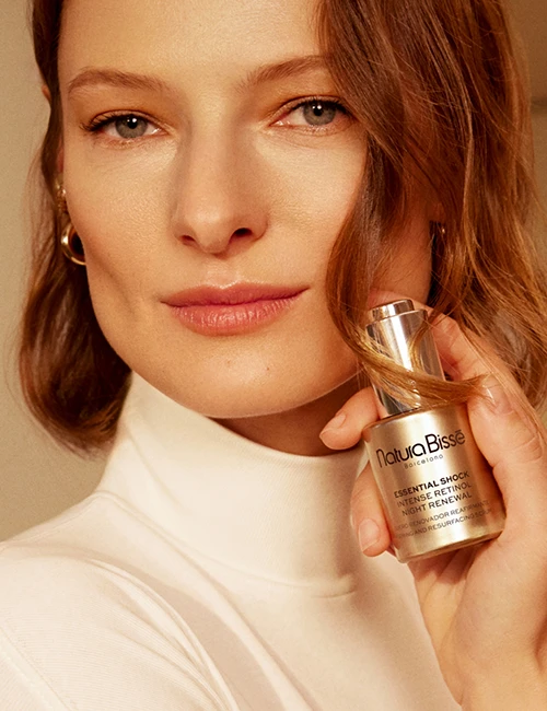 Mujer sonriendo y sosteniendo Essential Shock Intense Retinol Night Renewal frente a su cara. Producto presentado en nuestros bestsellers.