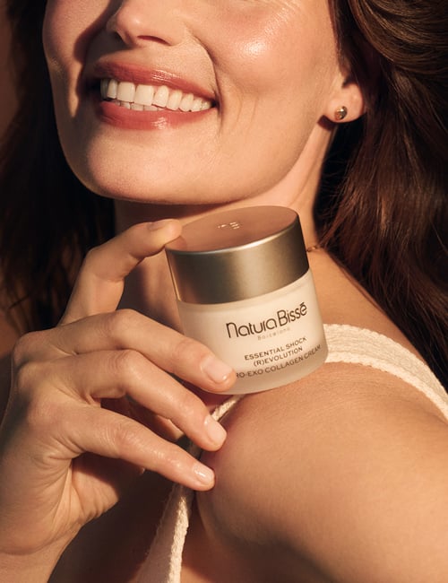 Mujer sonriendo sosteniendo la crema Essential Shock Revolution Pro-Exo Collagen Cream en sus manos. Producto presentado en nuestros bestsellers.