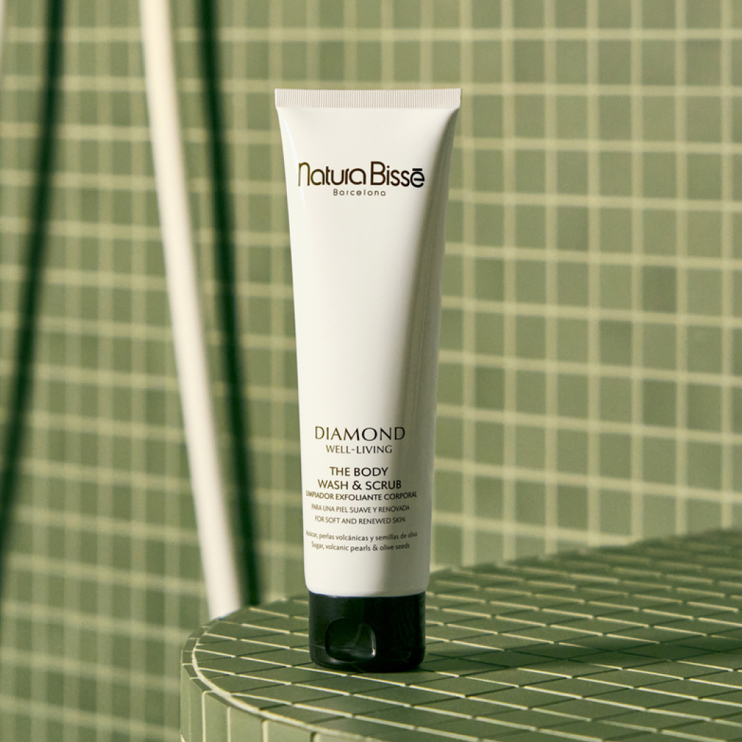 Exfoliante y limpiador corporal de Natura Bissé sobre fondo de baño con azulejos verdes