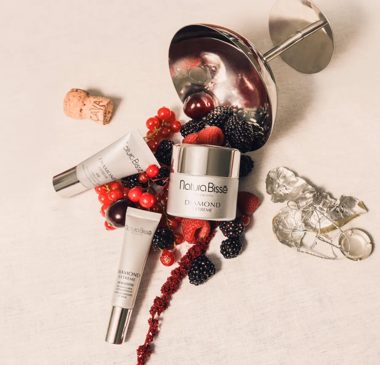 Los productos de Natura Bissé: Diamond Extreme Cream, Diamond Extreme Eye y Diamond Lip Booster están apoyados sobre frutos rojos en una mesa